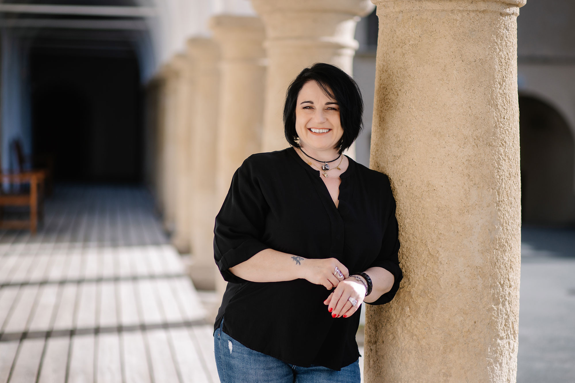 Nicole Oberhofer FotoGrafin lehnt sich lässig gegen eine Säule.