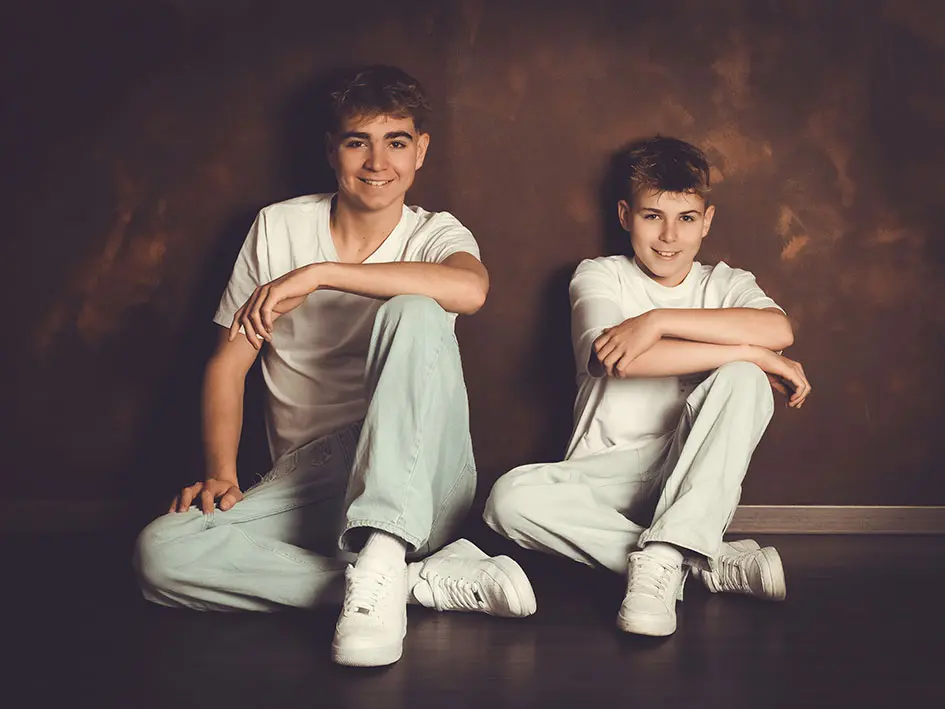 Zwei Burschen sitzen in jeans und weißen T-Shirt am boden vor einer rostigen Wand